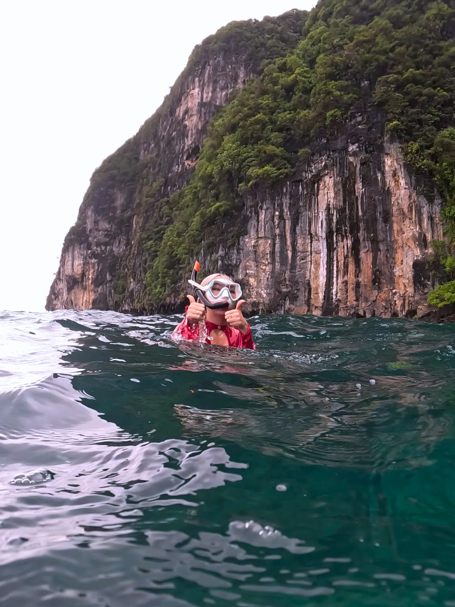 Traveler snorkeling in clear water beneath Phi Phi cliffs