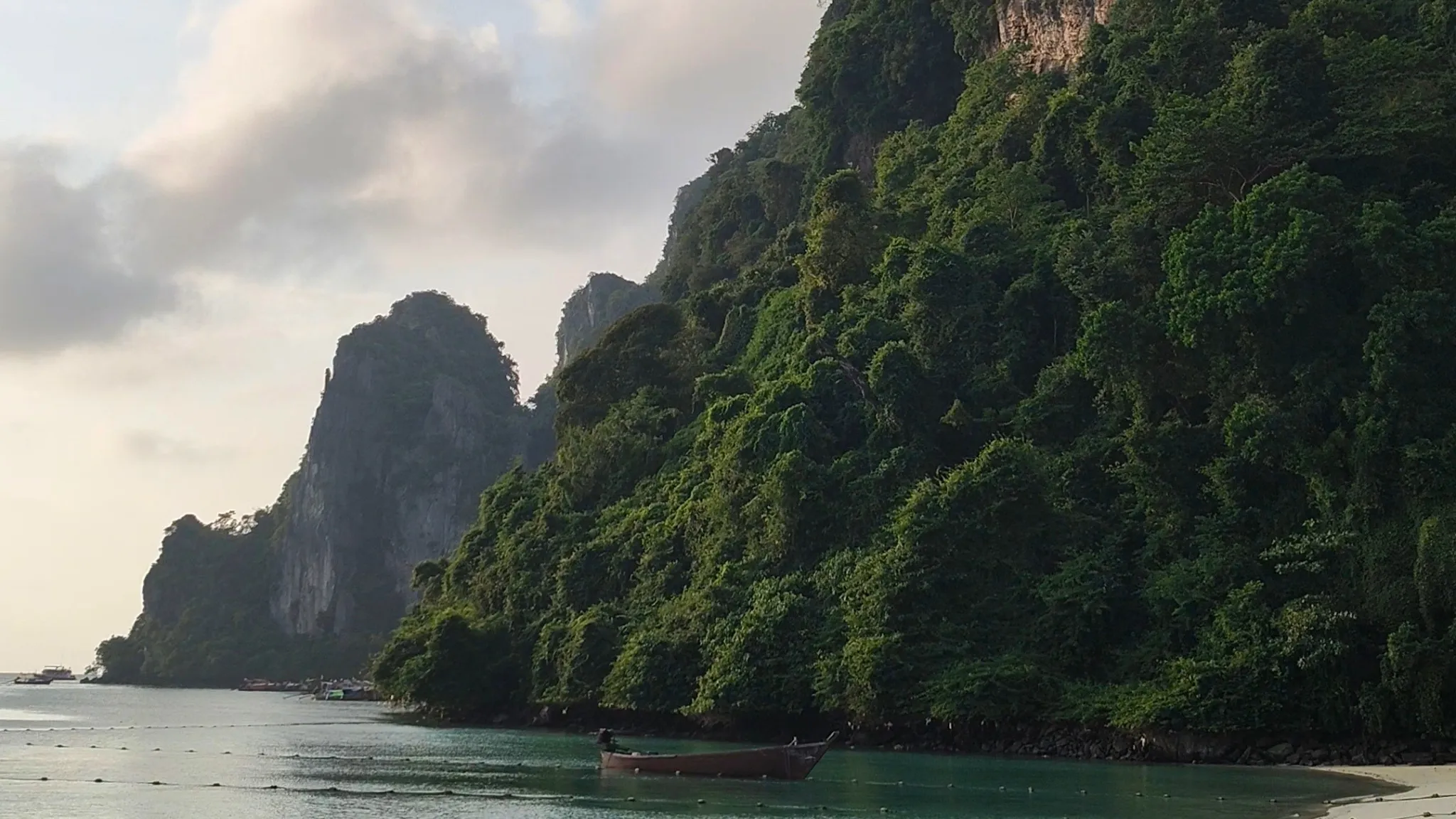 Longtail boat below a forested limestone cliff in Phi Phi