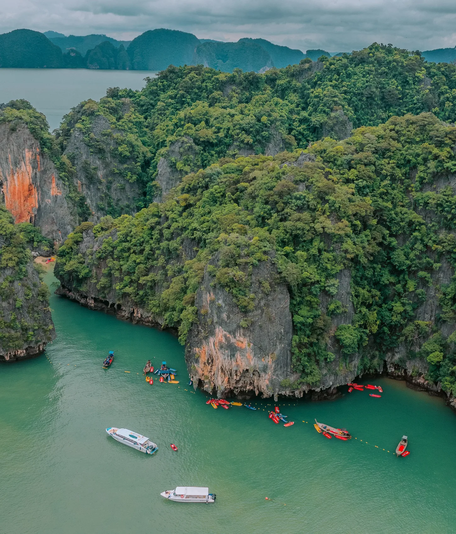 Canoes and boats beside towering limestone cliffs in Phang Nga Bay